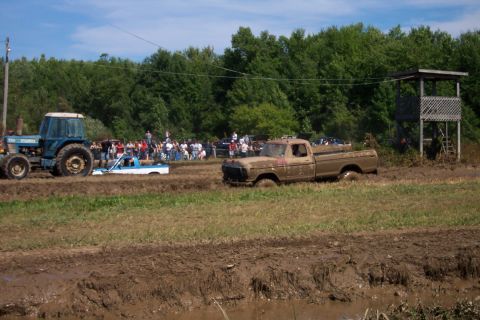 1979 Ford F-150 - A muddy 1970s pickup truck is stuck in a mud pit during a competition, with a tractor and another truck visible in the background.