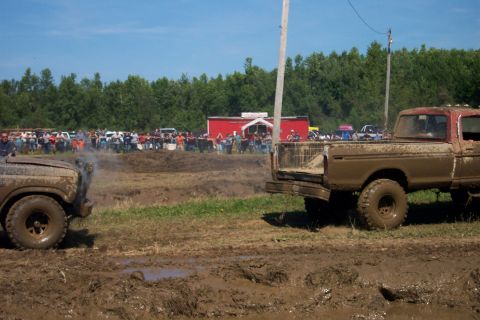 1979 Ford F-150 - Two muddy pickup trucks compete in a mud bog event, with spectators watching in the background.