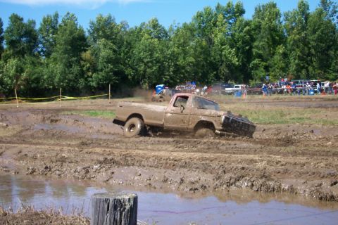 1979 Ford F-150 - Ford F-150 truck struggling through a muddy track during an event with onlookers watching.
