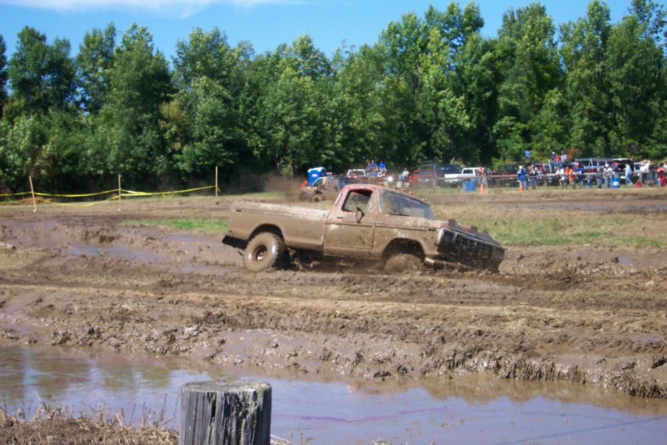 Mud-covered 1977 Ford F-150 stuck in a mud pit with spectators in the background