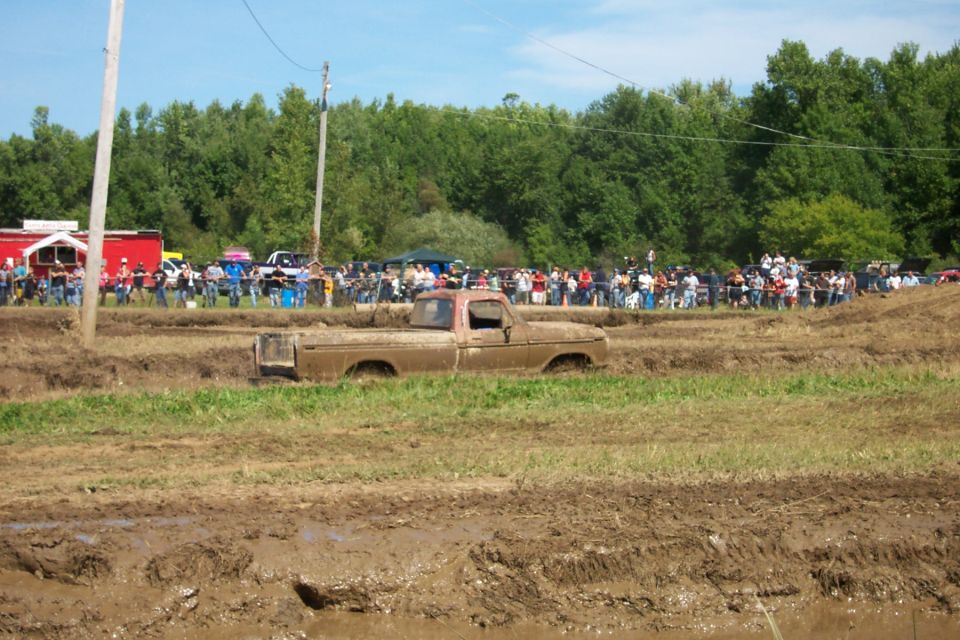 Muddy pickup truck stuck in a mud pit with a crowd watching