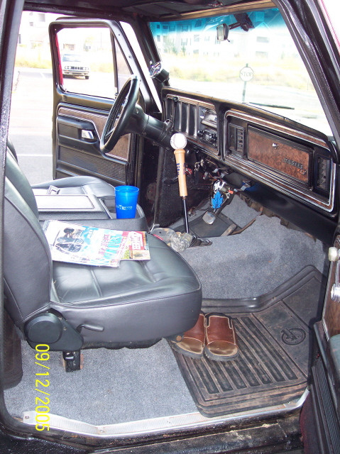1979 Ford Bronco - Interior of a classic Ford truck shot from the passenger side across a black vinyl bench seat, showing a woodgrain dash with rectangular ga…