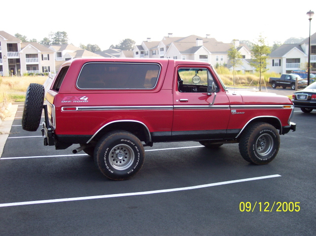Red 1979 Ford Bronco parked in a lot, spare tire mounted on the back