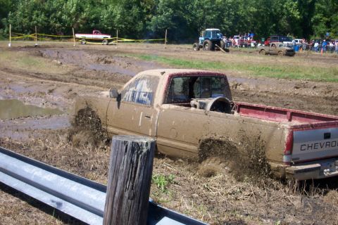 1979 Ford F-150 - Mud bogging event with a Chevrolet pickup truck stuck in the mire. Other vehicles and spectators are visible.