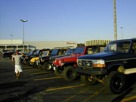 1993 Ford Bronco - A line of SUVs, including a dark green Ford Bronco, are parked in a lot under a clear sky.