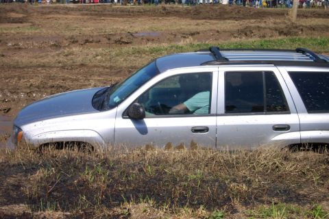 1979 Ford F-150 - A silver SUV is stuck deep in the mud, with onlookers visible in the background.
