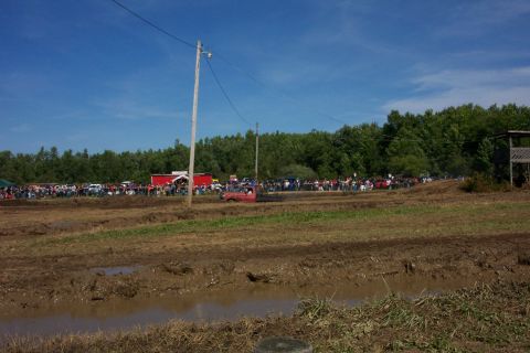 1979 Ford F-150 - Spectators gather to watch vehicles navigate a muddy track under a clear blue sky.