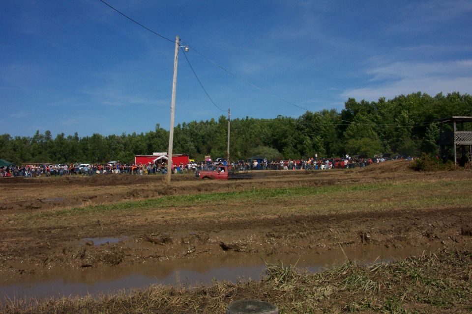 Crowd watches trucks in a muddy field during a mud bogging event