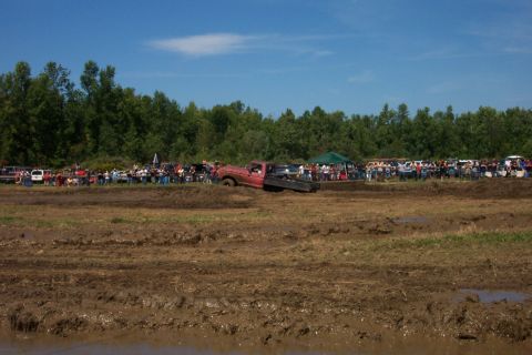 1979 Ford F-150 - A red pickup truck is stuck in a muddy field with spectators gathered.