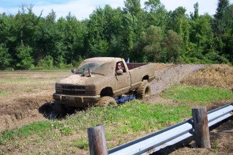 1979 Ford F-150 - Mud-covered pickup truck navigates a challenging mud pit, with a driver visible behind the wheel.