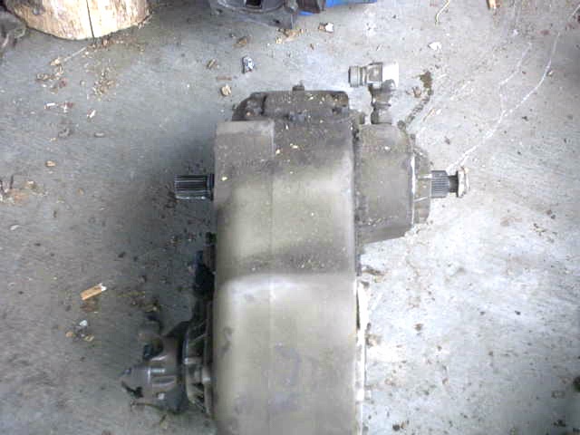 Gray transfer case with splined shafts on both ends, resting on a concrete floor