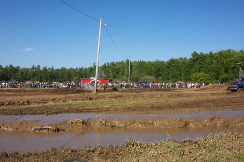 1979 Ford F-150 - A muddy field is filled with spectators and vehicles, with a blue truck visible on the right side of the frame.
