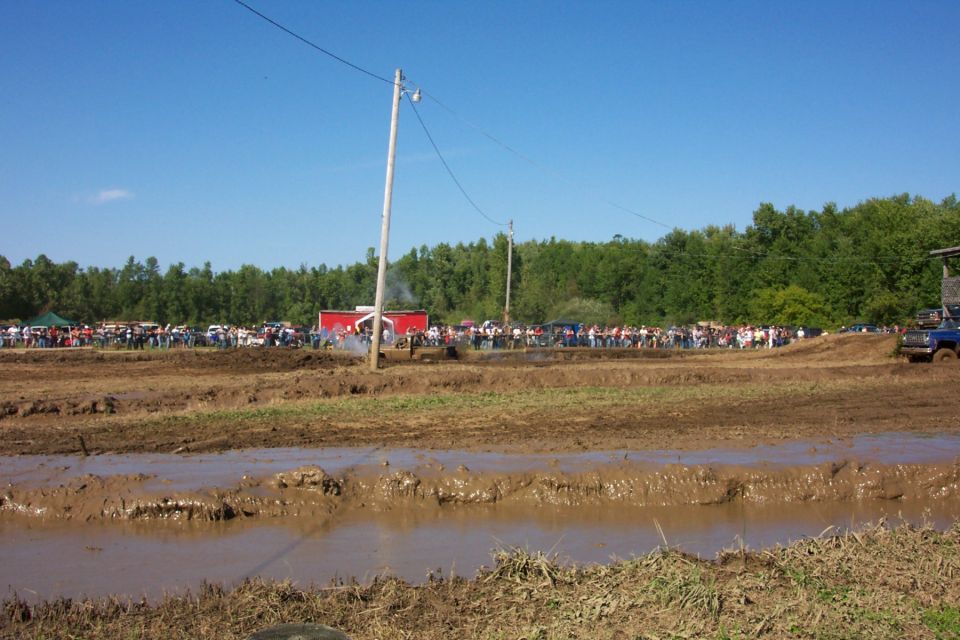 Muddy field with spectators and vehicles, blue truck on right