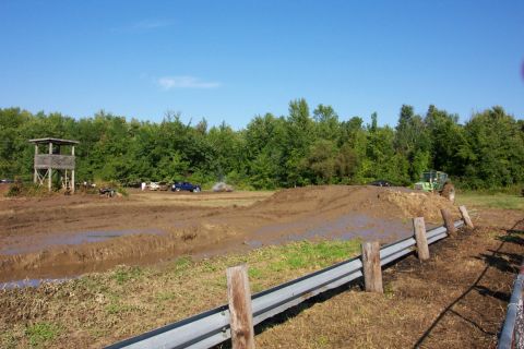 1979 Ford F-150 - Vehicles navigate a muddy track with a dirt mound and guardrails under a clear blue sky.