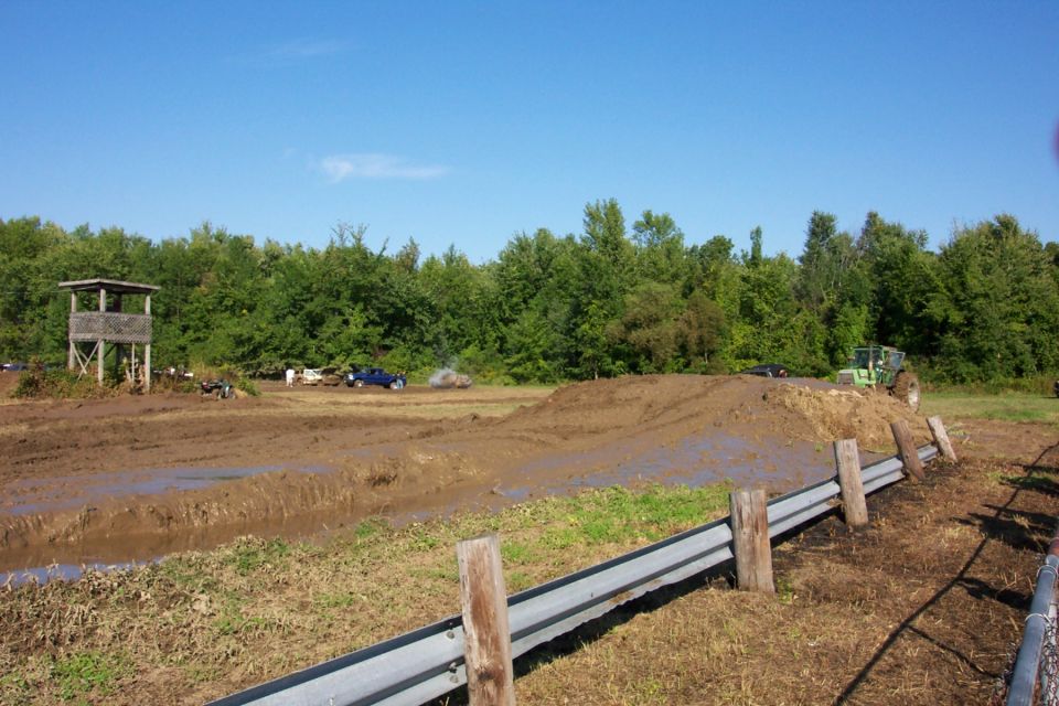 Muddy off-road course with a blue truck and a green tractor, plus a wooden observation tower