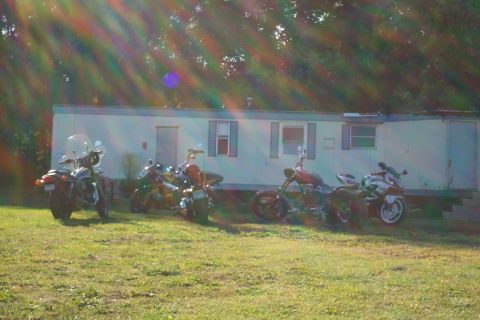 1979 Ford F-150 - Several motorcycles are parked on a grassy lawn in front of a white mobile home under a sun-drenched sky.