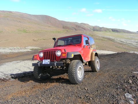 2001 Jeep Wrangler - This red Jeep TJ is parked on a rocky, dirt path with a scenic, hilly landscape under a blue sky.