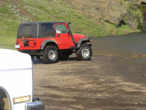 2001 Jeep Wrangler - A red 2001 Jeep TJ with a snorkel attachment is parked near a body of water, with another vehicle partially visible in the foreground.