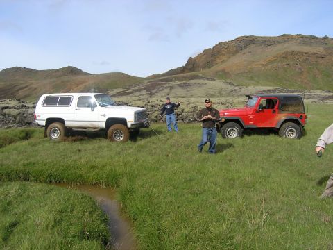 2001 Jeep Wrangler - Two off-road vehicles are parked in a grassy field with hills in the background.