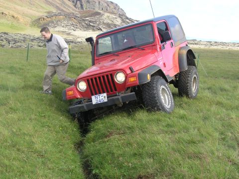 2001 Jeep Wrangler - A red Jeep TJ navigates a grassy incline, with a man observing its progress.
