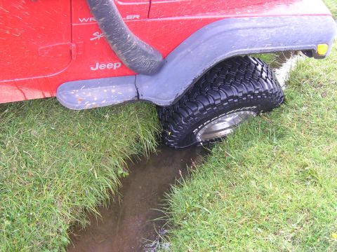 2001 Jeep Wrangler - A red 2001 Jeep TJ Wrangler navigates a muddy ditch off-road, its snorkel and aggressive tires.