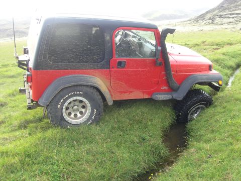 2001 Jeep Wrangler - Red 2001 Jeep TJ with snorkel stuck in a grassy ditch, front wheel submerged.