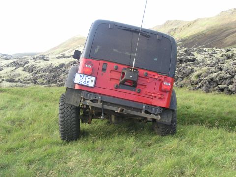 2001 Jeep Wrangler - A red Jeep Wrangler is parked on a grassy slope with a rocky, mountainous landscape behind it.