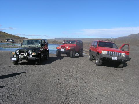 2001 Jeep Wrangler - Three Jeep SUVs, including a 2001 Jeep TJ, are parked on a rocky shoreline under a clear blue sky.