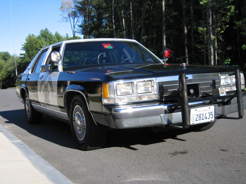 Black-and-white Ford police-style sedan with brush guard parked roadside