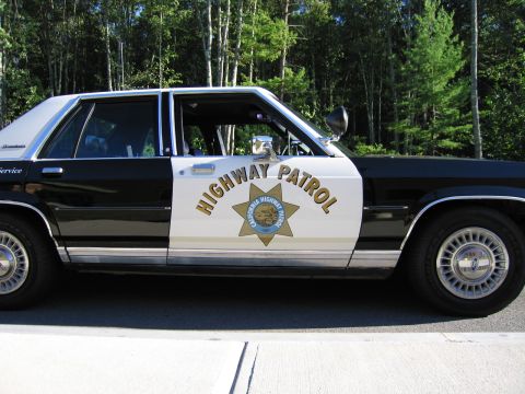 1991 Ford LTD Crown Victoria - Profile view of a black-and-white police-replica sedan showing HIGHWAY PATROL lettering and a gold star emblem on the door.