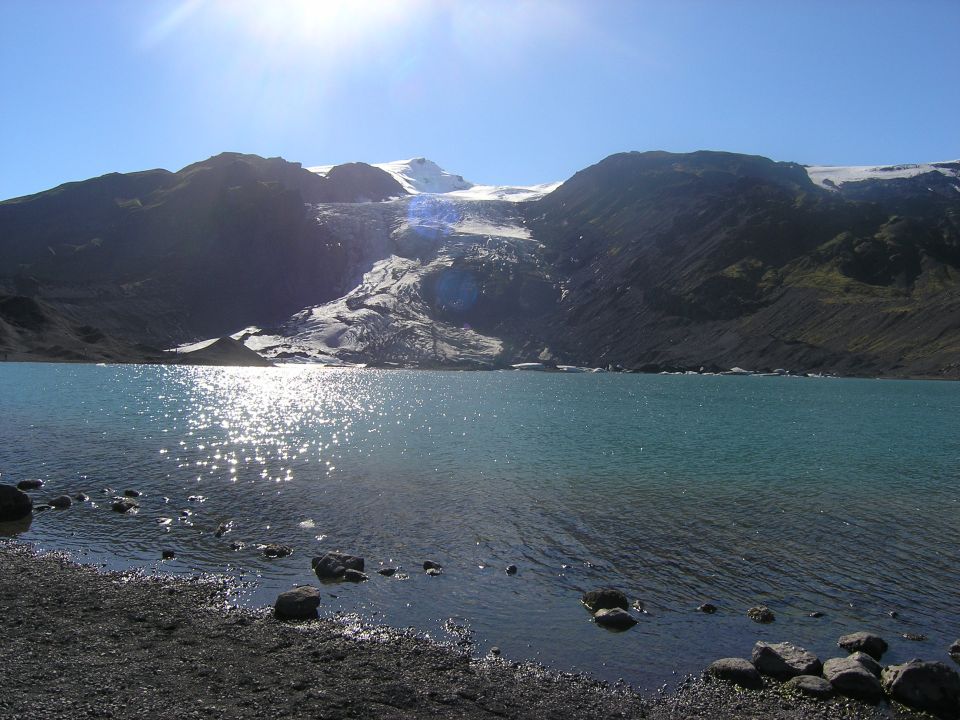 Glacier on a mountain overlooking a bright blue lake with sun glare on the water