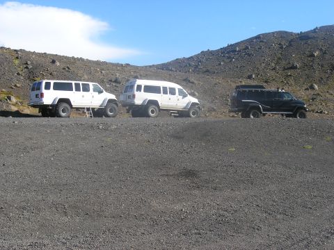 2001 Jeep Wrangler - Several modified vans and SUVs are parked on a desolate, rocky hillside under a bright blue sky.