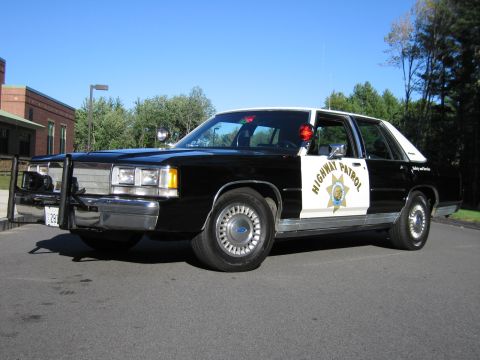 1991 Ford LTD Crown Victoria - black-and-white Ford Highway Patrol replica sedan with a brush-guard push bumper and door spotlight on a paved lot.