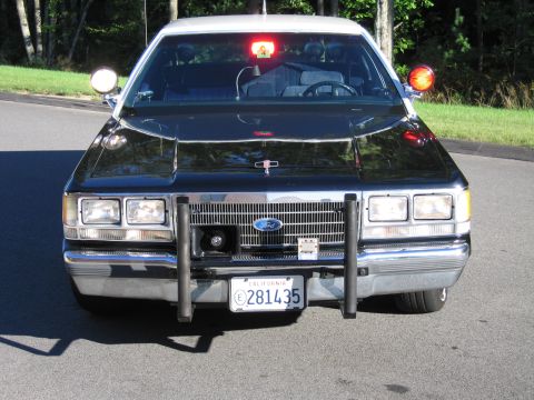 1991 Ford LTD Crown Victoria - Front view of a black Ford police-replica sedan with the Ford grille emblem, dual headlights, push bumper, and California plate.