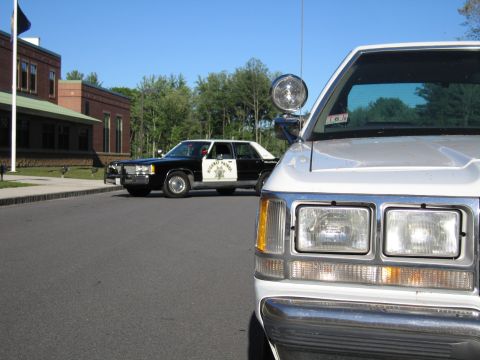 1991 Ford LTD Crown Victoria - silver vehicle's hood and headlights fill the foreground while a black-and-white Highway Patrol sedan sits parked behind on the lot.