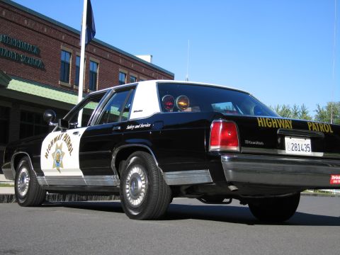 1991 Ford LTD Crown Victoria - Low rear three-quarter view of a black-and-white Highway Patrol police sedan with California plate 281435 parked by a brick school.