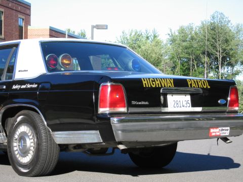 1991 Ford LTD Crown Victoria - Rear three-quarter view of a black-and-white Highway Patrol sedan with red roof beacons, an LTD Crown Victoria badge, and California plate.