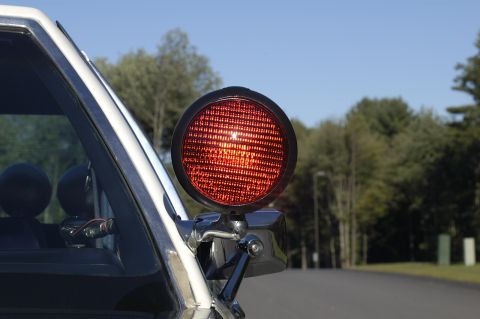 1991 Ford Crown Victoria - Red spotlight on the side of a police vehicle with trees and a blue sky in the background.