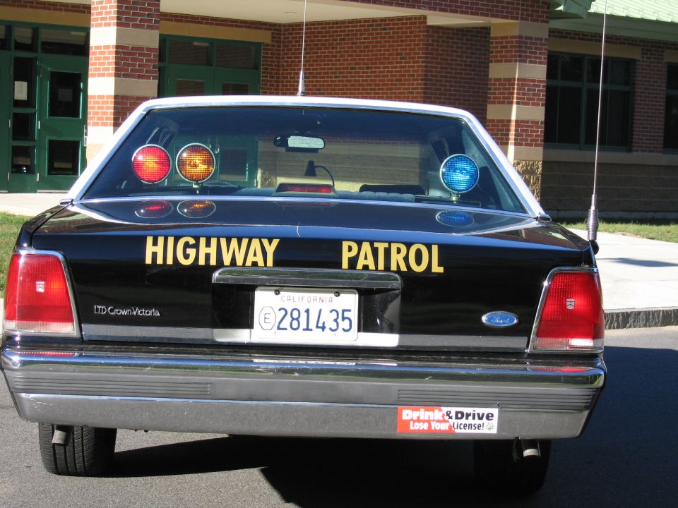 Rear view of a black Highway Patrol LTD Crown Victoria sedan with lit roof beacons