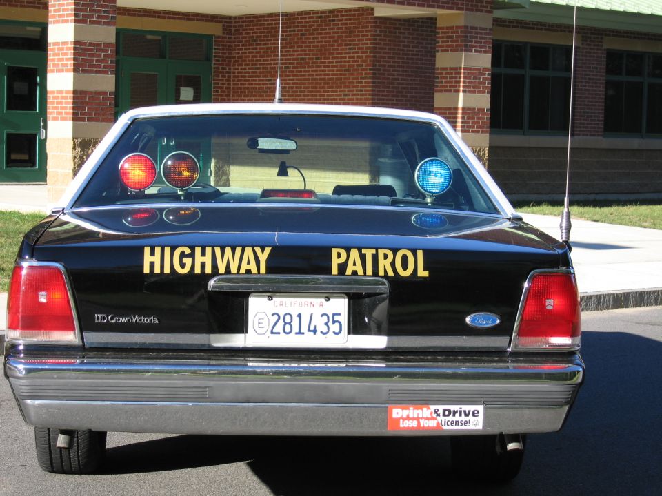 Rear view of a black Highway Patrol LTD Crown Victoria sedan outside a brick school