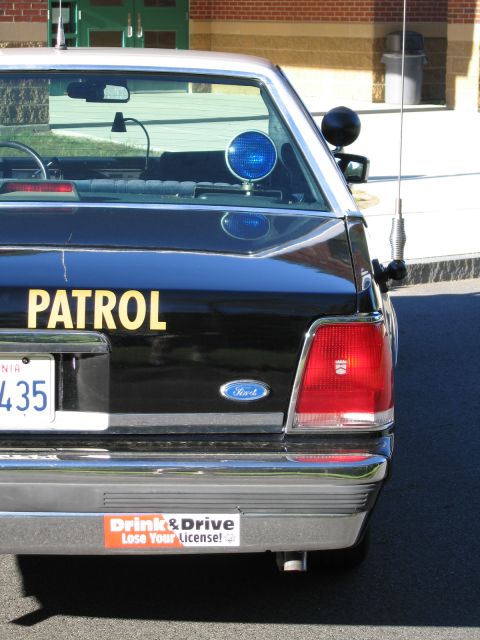 1991 Ford LTD Crown Victoria - Close-up of a black Ford police car's trunk lid showing yellow PATROL lettering, a blue roof light, Ford emblem and an anti-drinking-and-dr…