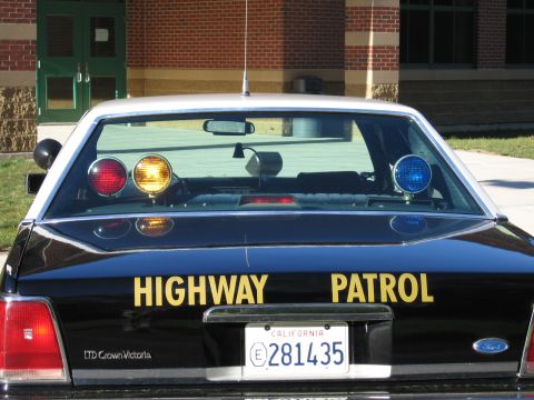1991 Ford LTD Crown Victoria - Rear view of a black Ford LTD Crown Victoria police car with yellow HIGHWAY PATROL lettering, roof lights and California plate 281435.