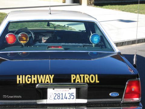 1991 Ford LTD Crown Victoria - Rear of a black Ford LTD Crown Victoria police car with red, amber and blue roof lights, HIGHWAY PATROL lettering and California plate 2814…