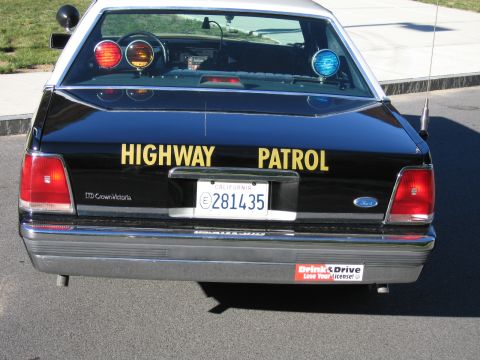 1991 Ford LTD Crown Victoria - Straight-on rear view of a black Ford LTD Crown Victoria police car with yellow HIGHWAY PATROL lettering, roof lights and California plate…
