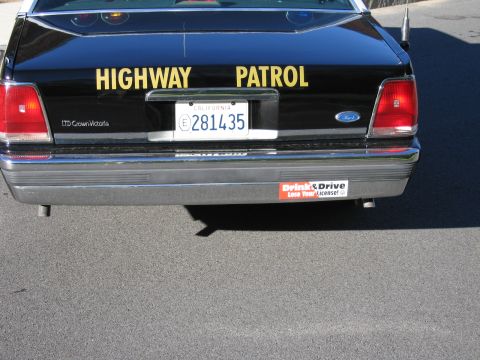 1991 Ford LTD Crown Victoria - Lower rear bumper of a black Ford police car with yellow HIGHWAY PATROL lettering, California plate 281435 and a bumper sticker.
