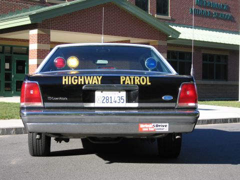 1991 Ford LTD Crown Victoria - Rear of a black Ford police car with HIGHWAY PATROL lettering and CA plate 281435, parked in front of a building reading Merrimack Middle S…