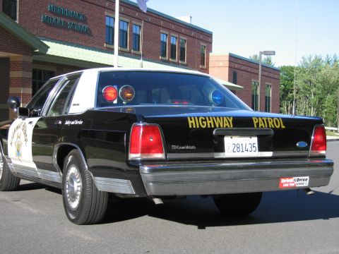 1991 Ford LTD Crown Victoria - Rear three-quarter view of a black-and-white Ford LTD Crown Victoria patrol car with a star emblem on the door and roof lights, outside a s…