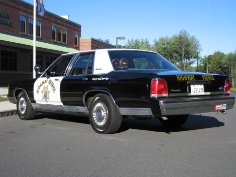 1991 Ford LTD Crown Victoria - Rear three-quarter view of a black-and-white Ford patrol sedan with HIGHWAY PATROL lettering, a gold star door emblem and roof lights.