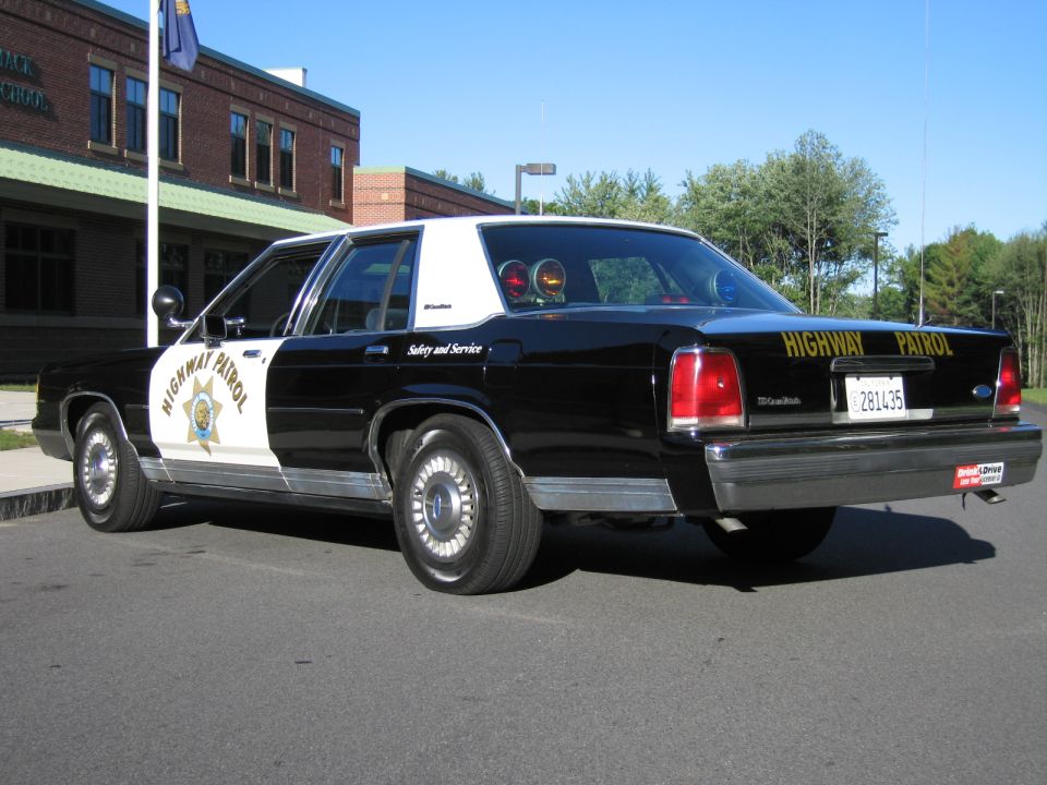 Rear quarter of black-and-white highway patrol sedan with door star emblem