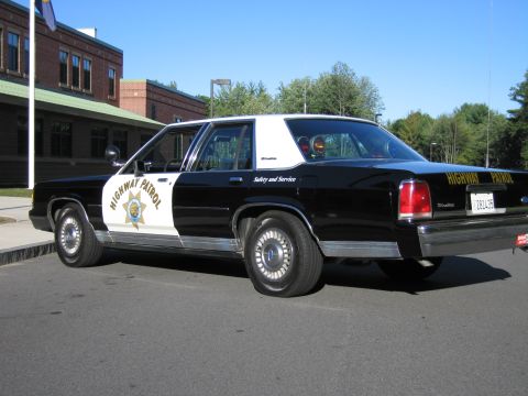 1991 Ford LTD Crown Victoria - Side rear-quarter view of a black-and-white Ford patrol sedan with HIGHWAY PATROL door lettering and a gold star emblem.